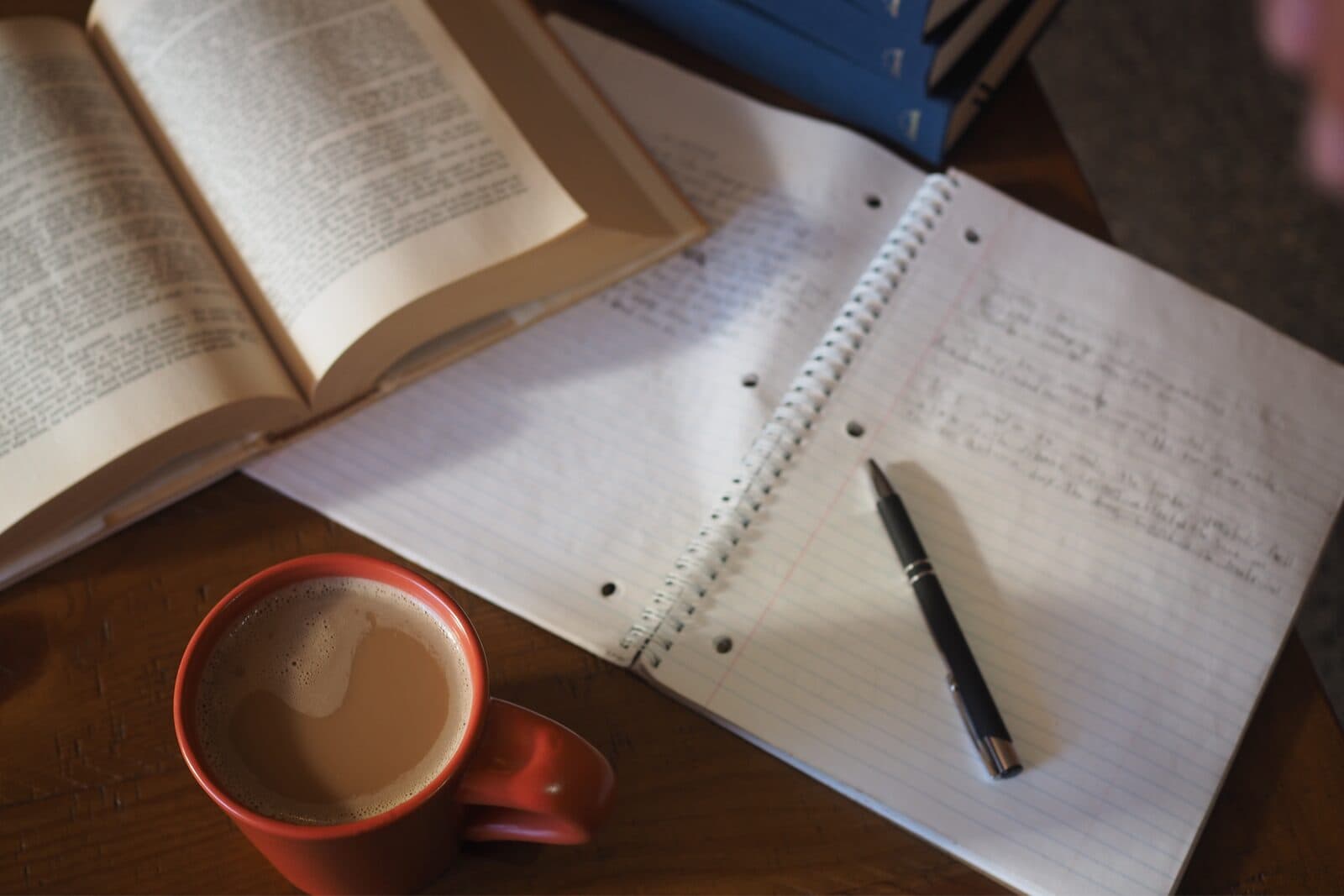 An open book, handwritten notebook, red coffee mug, and pen on a wooden table, representing quiet reflection and intentional planning for the next chapter of a business