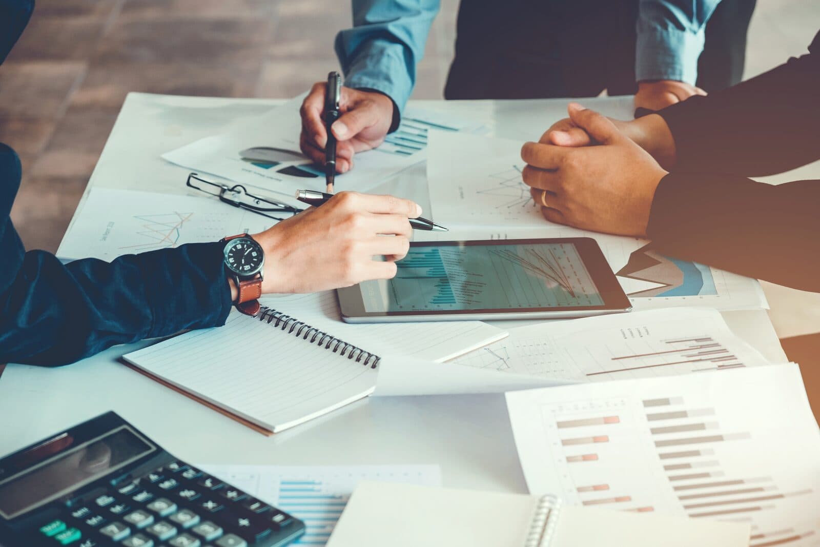Business professionals reviewing financial charts, graphs, and data visualizations on printed reports and a tablet during a detailed analysis meeting