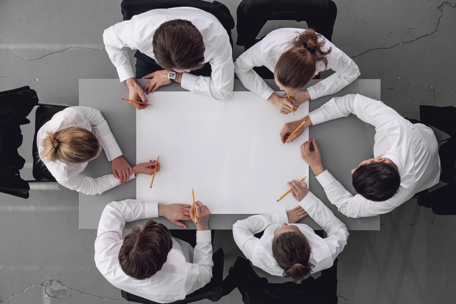 Overhead view of a diverse team of business professionals collaborating around a large white table with a blank planning sheet and pencils during a strategy session